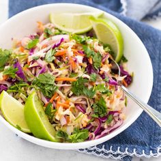 a white bowl filled with coleslaw and limes on top of a blue towel