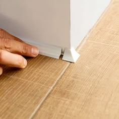 a person's hand on the edge of a wooden floor with a white corner