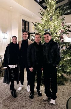 three men standing next to each other in front of a christmas tree with lights on it