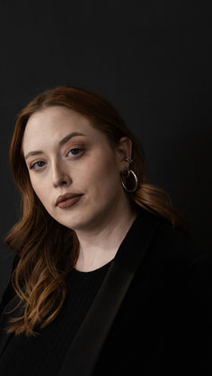 a woman with red hair and earrings on her head, looking off to the side