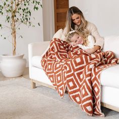 a woman sitting on a couch with a child wrapped in a blanket next to her