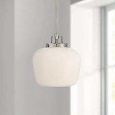 a white light hanging from a ceiling fixture in a room with large windows and gray walls