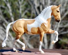 a toy horse that is standing on top of a wooden table with trees in the background