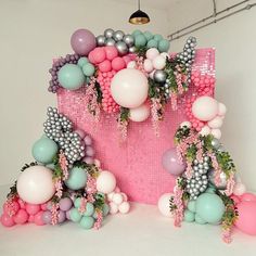 an arrangement of balloons and greenery on display in a white room with pink walls