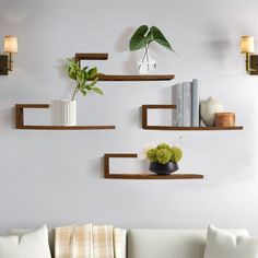 three wooden shelves on the wall above a white couch with pillows and flowers in vases