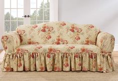 a floral couch with ruffles on it in front of a white wall and window