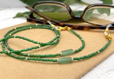 Shiny and bohemian eyeglass necklace chain in green tones with light flashes of gold, made with tiny  Preciosa Czech crystal seed beads and genuine green Jade gemstones.     Paired with beautiful tiny gold plated crystal seed beads, this delicate handmade eyeglass chain will definitely create a unique look. This eyeglass lanyard is made on strong quality beading wire with wire guardians that protect the quality eyeglass holder grips. The necklace is ended with spring clasps that hold the eyeglas Green Beaded Necklace With Adjustable Chain, Handmade Green Glasses Chains With Round Beads, Green Glass Festival Jewelry, Bohemian Green Glasses Chains, Green Bohemian Glasses Chains As Gift, Green Beaded Glasses Chain As Gift, Green Beaded Glasses Chain Gift, Green Beaded Chain Glasses For Gift, Green Glasses Chains With Round Beads For Gift