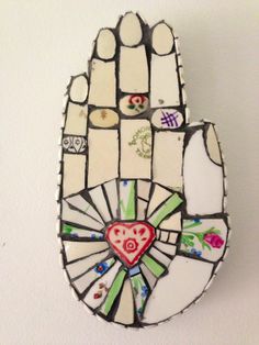 a stained glass hamsah hanging on the wall with hearts and flowers painted on it