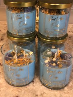 four jars filled with candles sitting on top of a marble counter next to each other