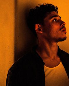 a young man leaning against a wall with his head turned to the side looking up