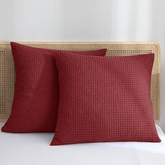 two red pillows sitting on top of a bed next to a wicker headboard