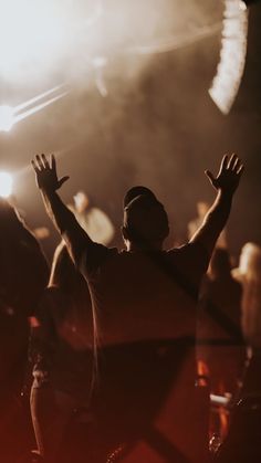 a man standing in front of a crowd at a music concert with his hands up