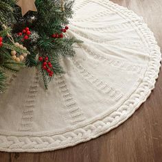 a christmas tree skirt on the floor with pine cones and red berries hanging from it