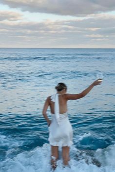 a woman standing in the ocean with a frisbee on her hand and looking at the water