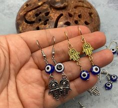 These Evil Eye and Hamsa Hand earrings set are handcrafted personally for me, Derlis. You can choose from 6 different styles on golden or silver tone finish. MATERIALS:   - Dark Blue Evil eye flat round bead, 8mm and 6mm(These resin beads are handmade so it is normal if the eye is a little inconsistent)  - Antique golden Hamsa hand spacer bead, Tibetan Alloy, 12x10mm, double-sided - Antique Silver Hamsa hand charm 20.5x 12.5mm, one-sided - Rhodium and gold finish fishhook earwires All materials Hand Earrings, Evil Eye Earrings, Hand Of Fatima, Blue Evil Eye, Eye Earrings, Resin Beads, Hamsa Hand, Organza Bags, Earrings Set