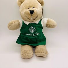 a brown teddy bear wearing a starbucks shirt and green overalls with the words hong kong on it