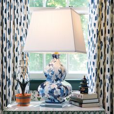 a blue and white vase sitting on top of a table next to a lamp in front of a window