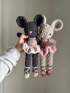 two crocheted mice hanging from strings in front of a white wall, one is holding the other