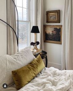 a bed with white sheets and pillows in front of a painting on the wall next to a window