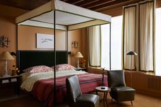 a bedroom with a four poster bed and two chairs in front of the large window