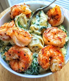 a bowl filled with pasta and shrimp on top of a wooden table