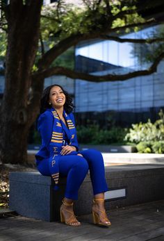 a woman sitting on top of a cement bench next to a tree and wearing blue