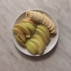 sliced apples and bananas on a white plate sitting on a marble counter top, ready to be eaten