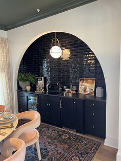 a dining room table and chairs in front of a black brick wall with an arched doorway