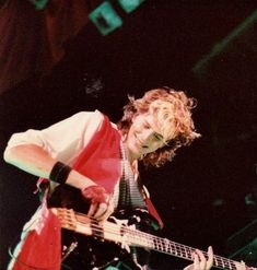 a young man with curly hair playing a bass guitar on stage at a music festival