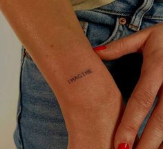 a woman's arm with the word imagine tattooed on her left wrist, in black ink