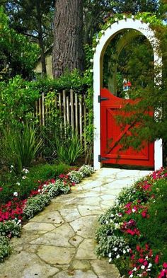 a red door in the middle of a garden with pink and white flowers around it