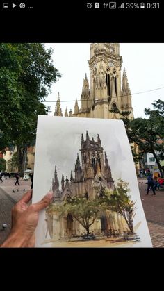 a person holding up a drawing in front of a building with a clock tower on it