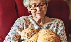 an older woman sitting in a red chair with her cat sleeping on the armrest