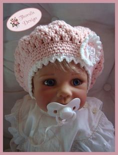 a baby doll wearing a pink crochet hat with a pacifier in it's mouth