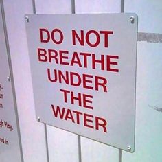 a do not breathe under the water sign attached to a white fence with red lettering