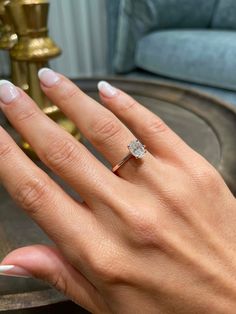 a woman's hand with a diamond ring on her finger, in front of a blue couch