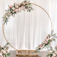 a wedding arch with pink flowers and greenery on the floor in front of a white curtain