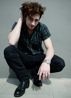 a young man sitting on the ground with his hand to his head and wearing black shoes