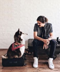 a woman sitting on top of a suitcase next to a dog wearing a bandana