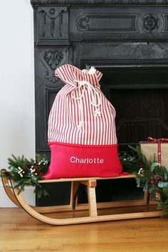 a red and white bag sitting on top of a wooden sleigh next to a fireplace