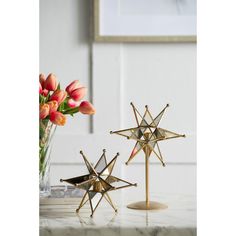 two gold star ornaments sitting on top of a marble table next to a vase filled with tulips