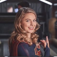 a woman in a superman costume pointing to the side with her finger up and smiling