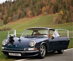 an old blue sports car parked on the side of the road in front of a green field