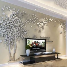 a living room with a tv and large tree wall art on the wall behind it