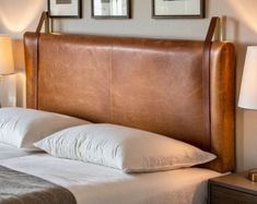 a bed with white pillows and brown leather headboard