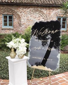 a welcome sign sitting on top of a white pedestal in front of a brick building