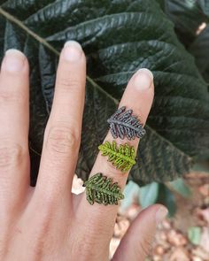 a person's hand holding a ring with leaves on it and two rings in the middle