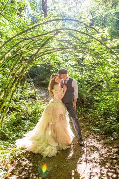 a bride and groom standing in the middle of a forest under an arch made of trees