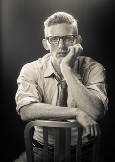 a black and white photo of a man sitting in a chair with his hand on his chin