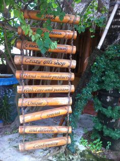 a wooden sign hanging from the side of a tree in front of a building with words written on it